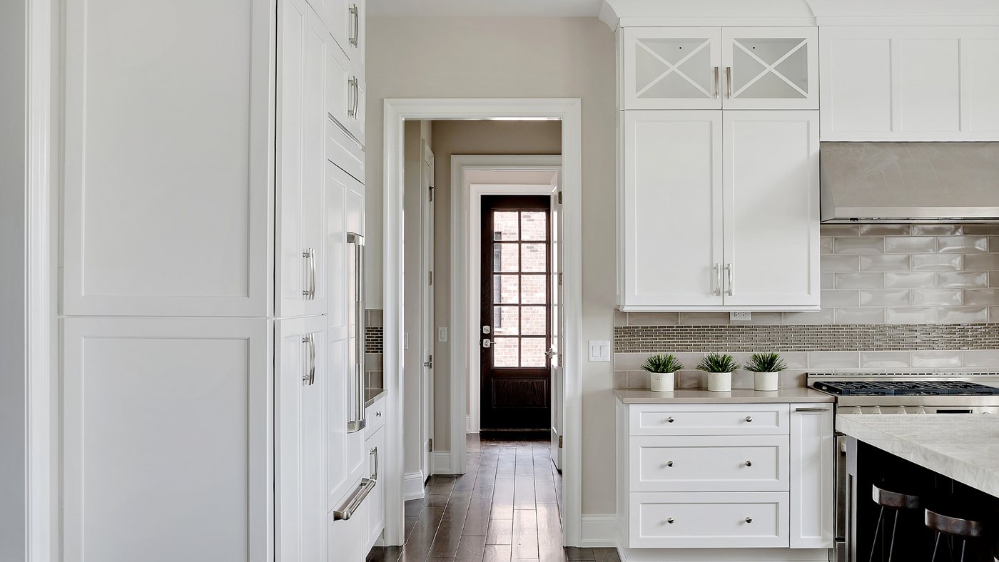 White kitchen with shaker cabinets and a range, seen through an open doorway