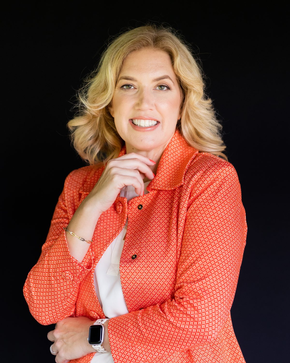 Portrait of Gina Graham in a coral jacket against a black background