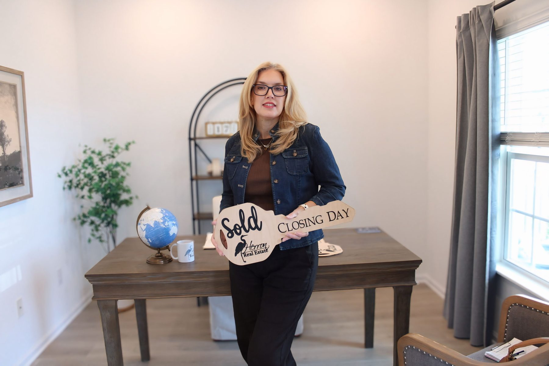 Gina Graham holding a wooden key-shaped sign reading Sold, Closing Day, with the Herron Real Estate logo